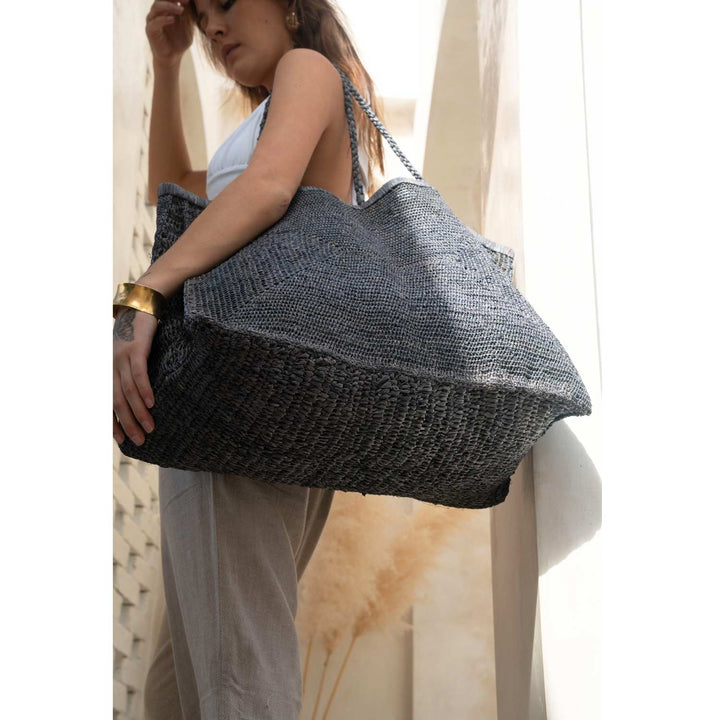 Woman carrying Clipa Raffia Beach Tote Bag, handmade in Madagascar, showcasing its natural texture and spacious design.