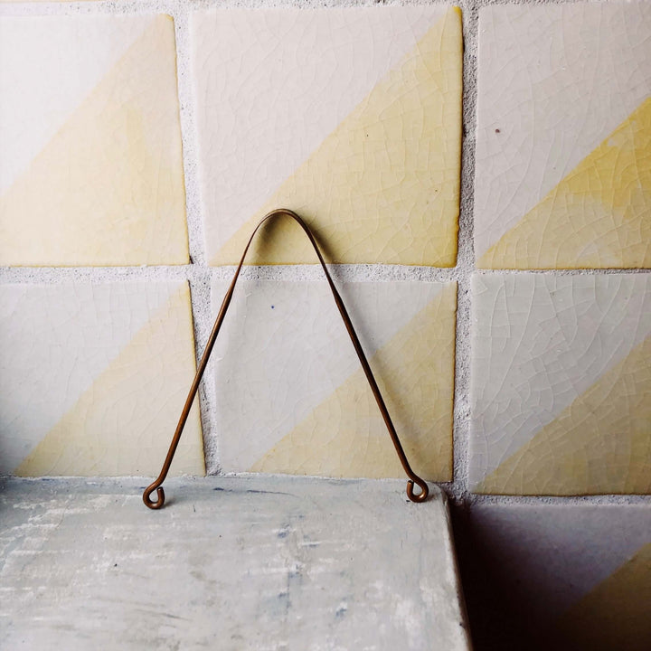 Copper tongue cleaner for Ayurvedic oral hygiene against yellow and grey tiled background.
