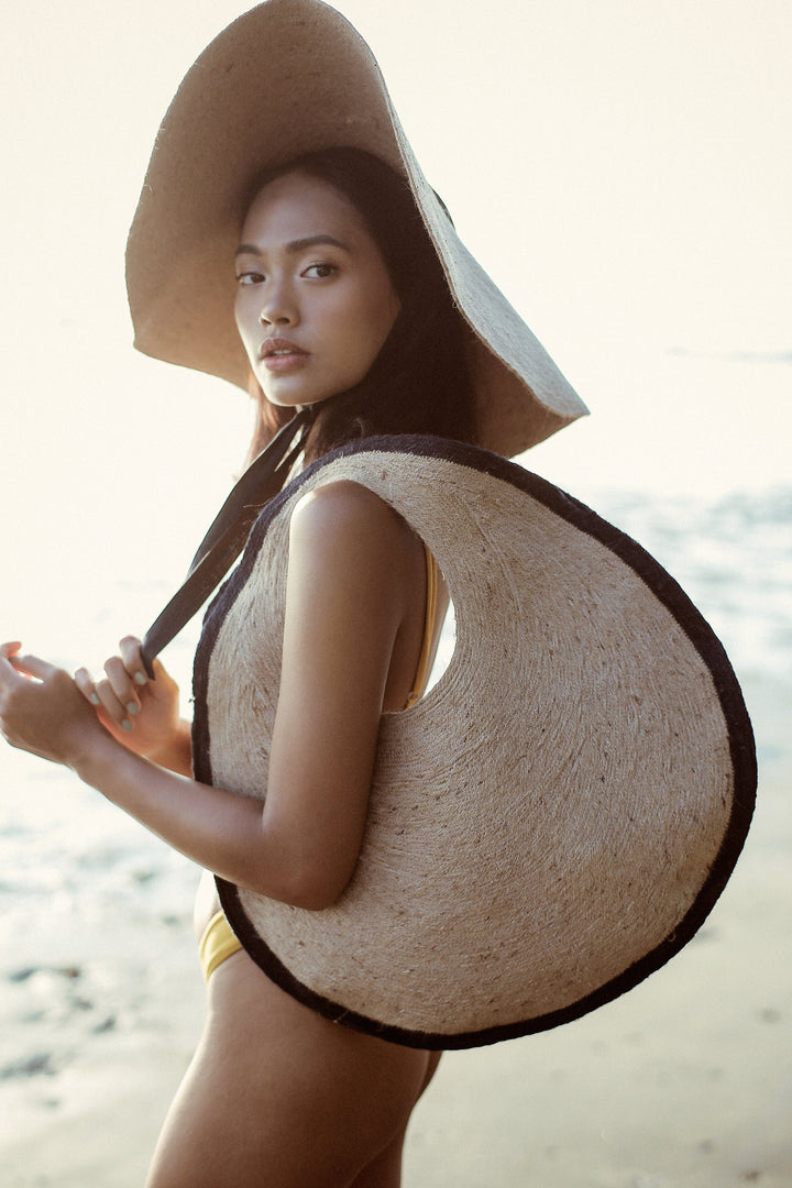 Woman on beach carrying Solo Halo Jute Bag in black and natural, featuring a bold circular design; perfect for stylish, eco-friendly living.