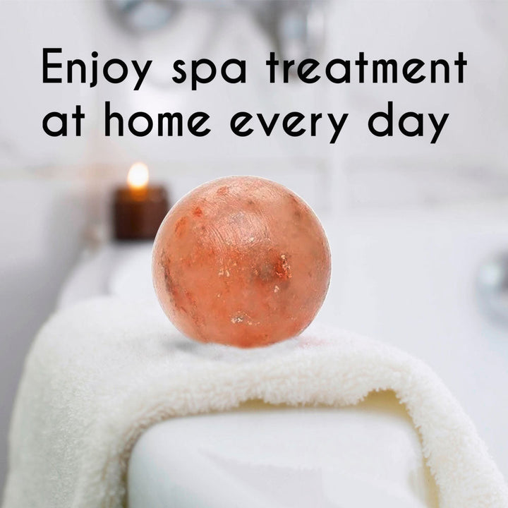 Himalayan Pink Salt Bath Ball on tub edge with candle, promoting spa-like relaxation at home.