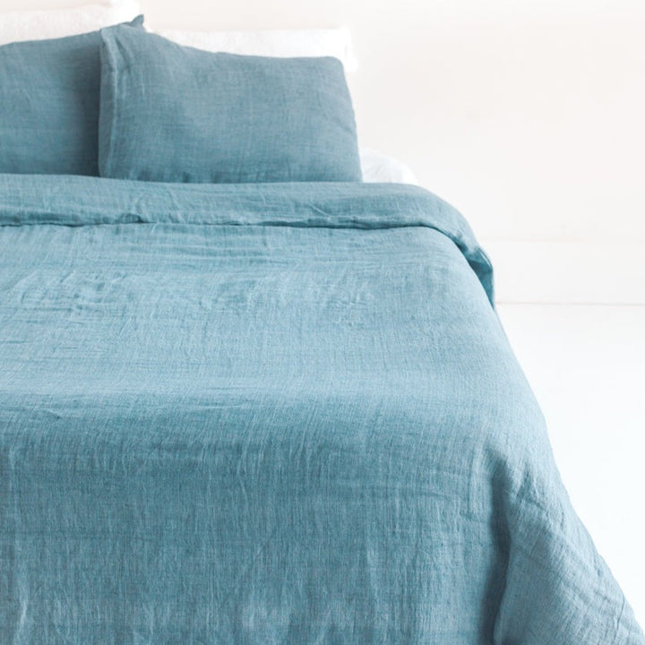 Denim blue linen duvet cover set made from Belgian flax, showcasing a woven, stonewashed texture on a bed.