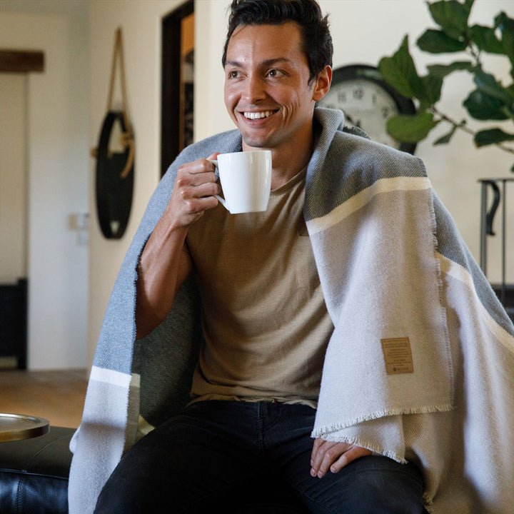 Man relaxing with a mug wrapped in a soft Peace Namaste Blanket, featuring a calming neutral palette and meaningful message tag.