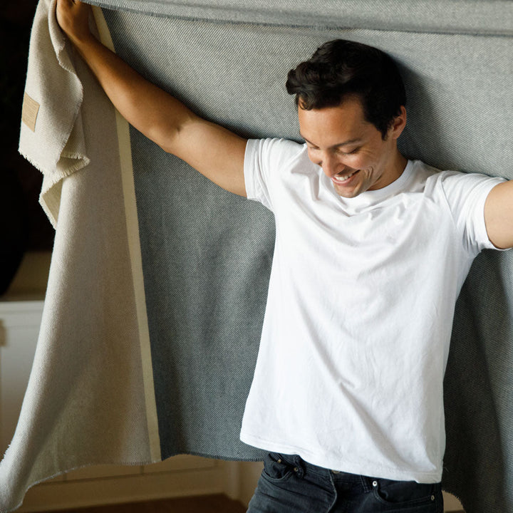 Man smiling and holding a Peace Namaste Blanket made of soft, breathable lambswool, showcasing its calming neutral palette and cozy texture.