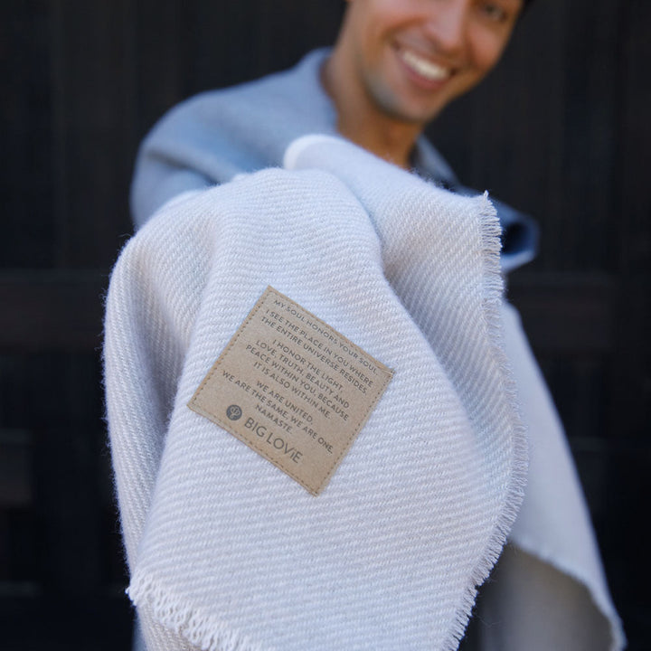 Person holding a soft, breathable Namaste Blanket with a heartfelt message tag, showcasing its calming neutral palette.