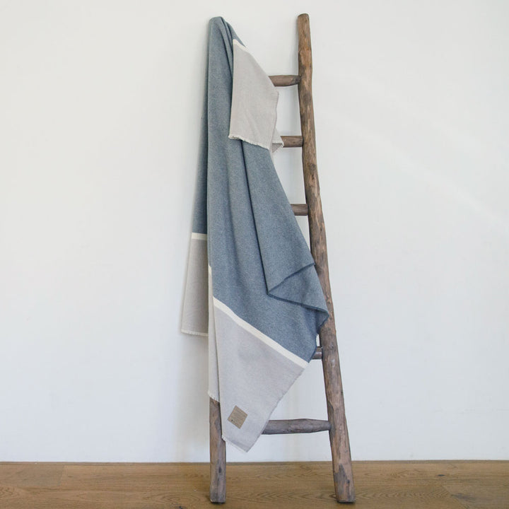 Namaste Blanket in soft, breathable lambswool with neutral tones, draped over a rustic wooden ladder showcasing a cozy design.