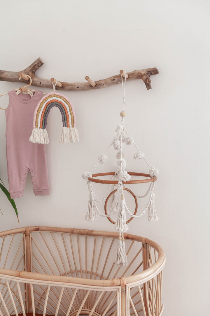 Handmade organic cotton pom pom mobile with macrame and rattan hanging over a baby crib, enhancing nursery decor.