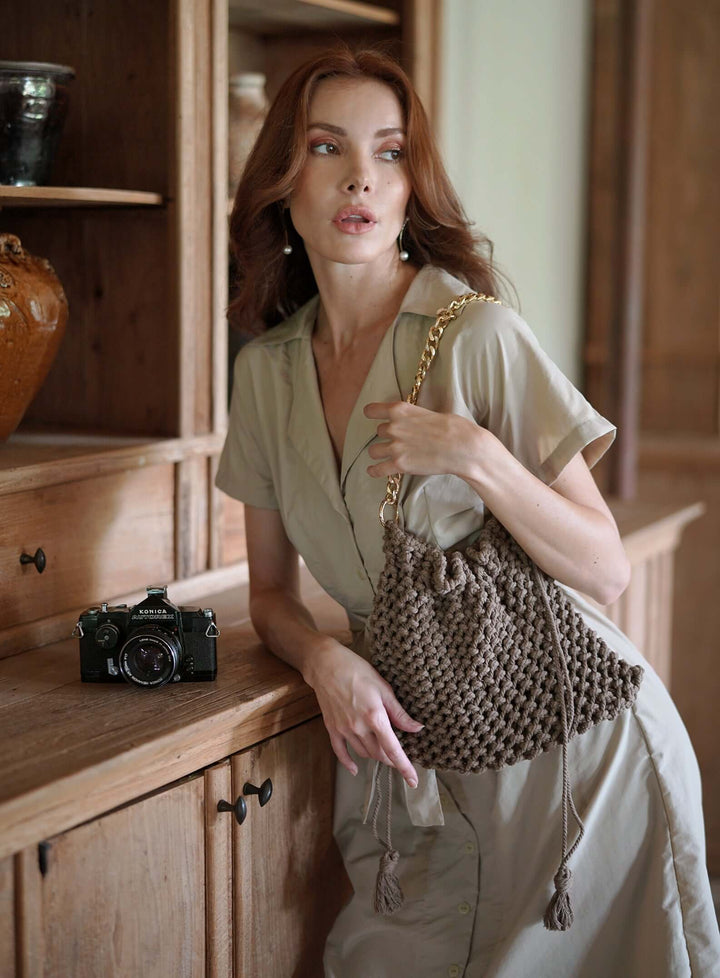Woman with Lyon Macrame Boho Tote Bag in toasted beige, featuring natural cotton and gold chain strap, handcrafted by artisans.