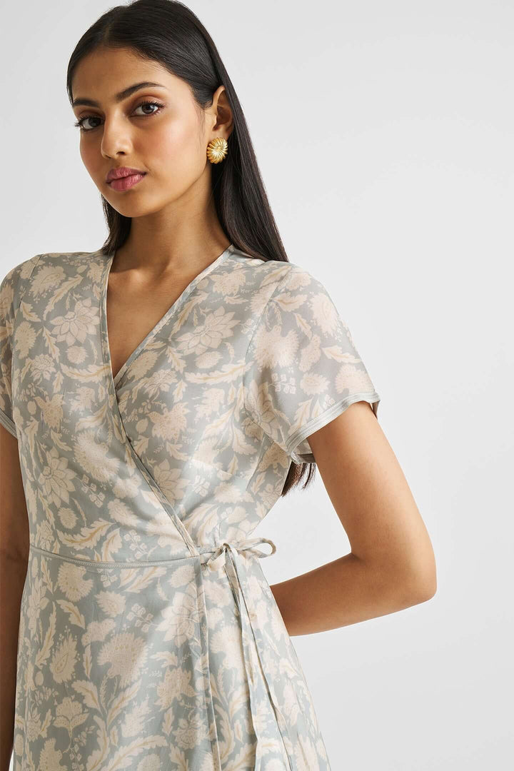 Woman wearing a floral maxi wrap dress in subtle blue with short sleeves and a tie at the waist, made from sustainable Bemberg™ crepe.