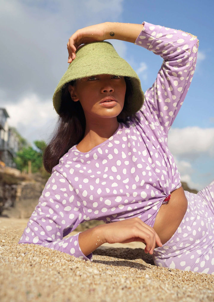 Woman wearing Naomi Jute Clochet Straw Hat in Matcha Green lounging on a sunny beach in a purple polka dot outfit.
