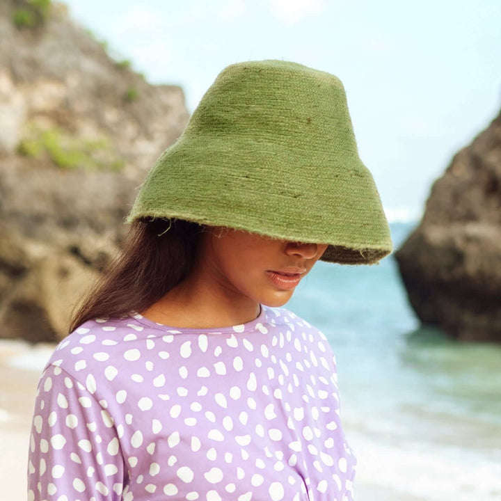 Woman wearing Naomi Jute Clochet Straw Hat in Matcha Green on a beach, handmade in Bali for sun protection with style and function