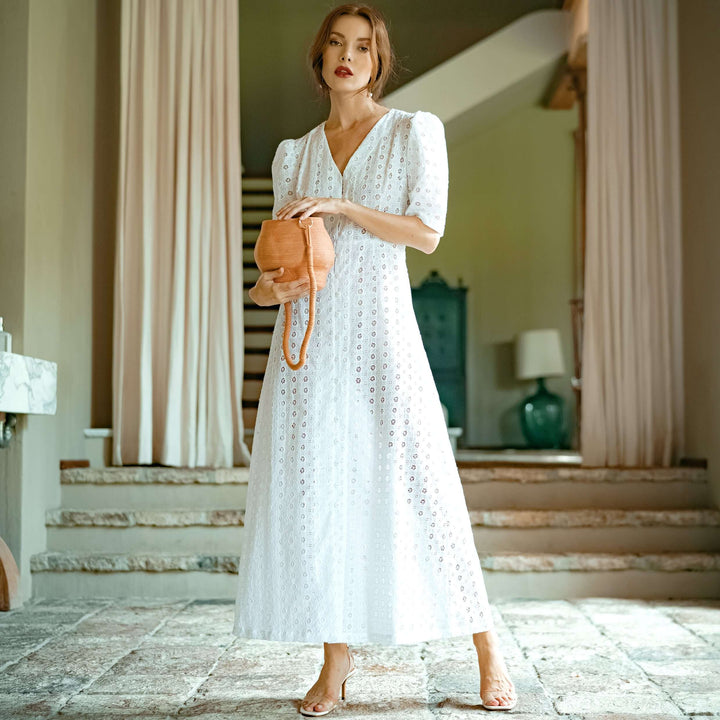 Woman wearing Olympia Embroidered Cotton Dress in white, handmade in Bali, inspired by vintage elegance, holding a tan handbag.