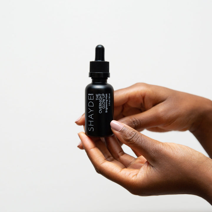 Person holding the Overnight Glow Up Mask bottle, an award-winning skincare product for dark spots and post-acne marks.