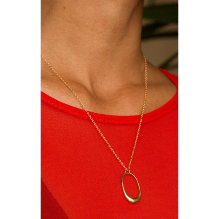 Woman wearing Delicate Mezi Brass Pendant Necklace with curvilinear charm on a simple chain, handcrafted by Kenyan artisans.