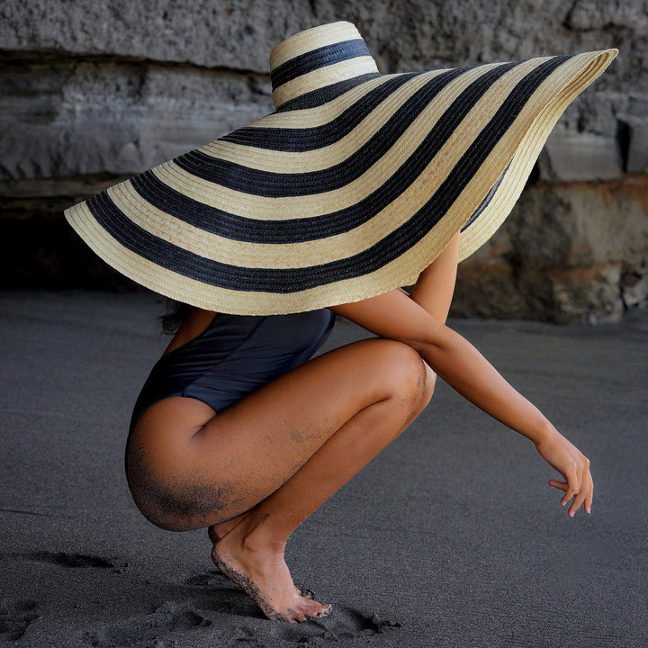 Solana Oversized Black and Natural Striped Straw Hat on beach, featuring dramatic handwoven design, perfect for sun protection and style.