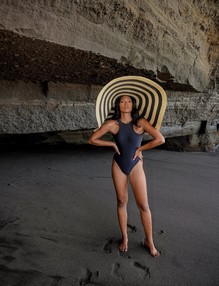Woman wearing Solana Oversized Striped Straw Hat in black & natural on a beach.