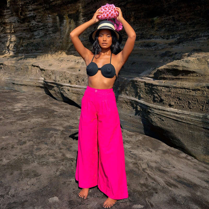 Woman wearing Taylor Wide-leg Palazzo Pants in bright pink on a rocky beach, posing with arms raised, showcasing the high-rise design.