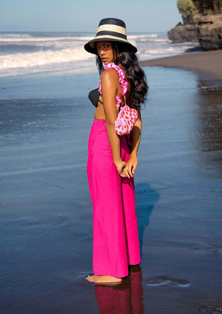 Woman in pink Taylor Wide-leg Palazzo Pants on a beach with hat and lei, enjoying a sunny day.