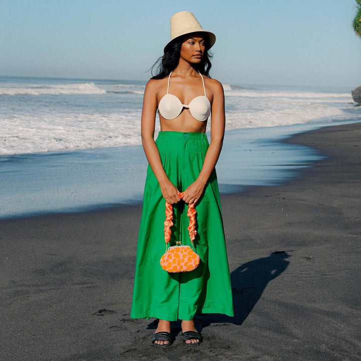 Woman wearing green wide-leg Palazzo pants with high-rise, standing on a beach with a hat and bikini top.
