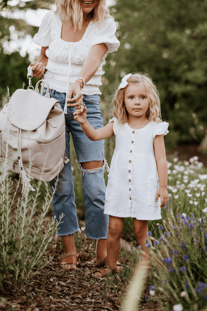 Woman holding child's hand with Citi Journey vegan leather diaper bag in a garden setting