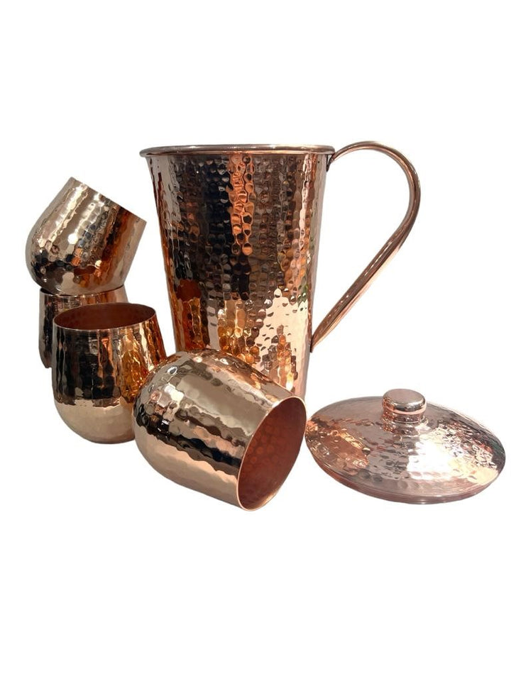 Hammered copper pitcher with lid and four shiny tumblers set, featuring a textured finish and elegant handle, perfect for serving.