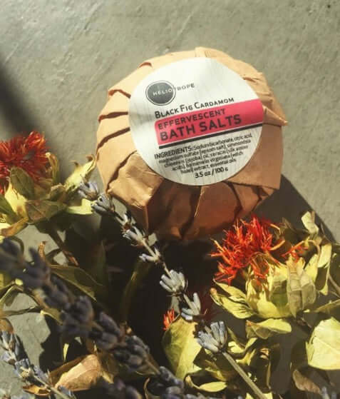 Effervescent bath salts wrapped in eco-friendly packaging next to dried flowers on a wooden surface.