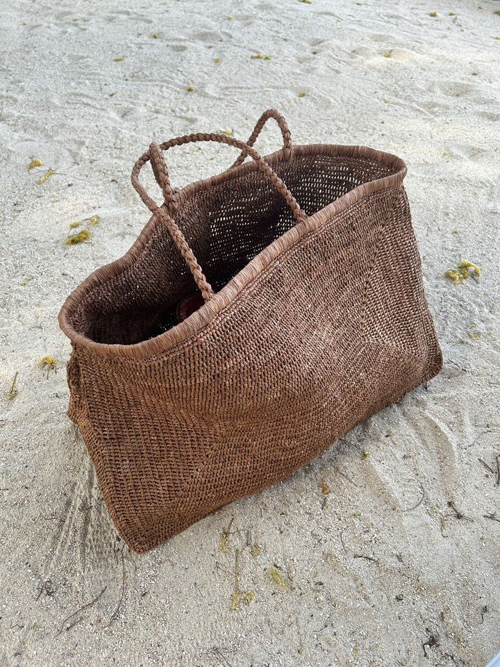 Handmade raffia beach tote bag on sandy beach, artisan crafted in Madagascar, ideal for stylish carryall needs.