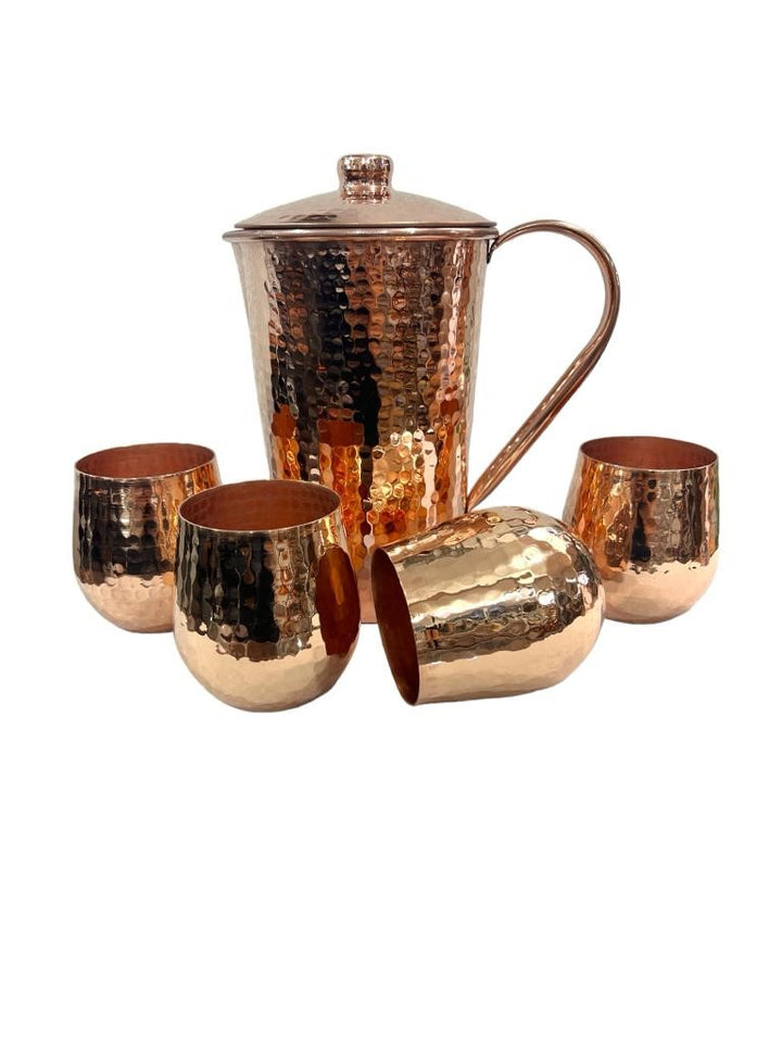 Hammered copper pitcher with lid and four shiny tumblers set, elegant drinkware with a polished finish, perfect for serving beverages.