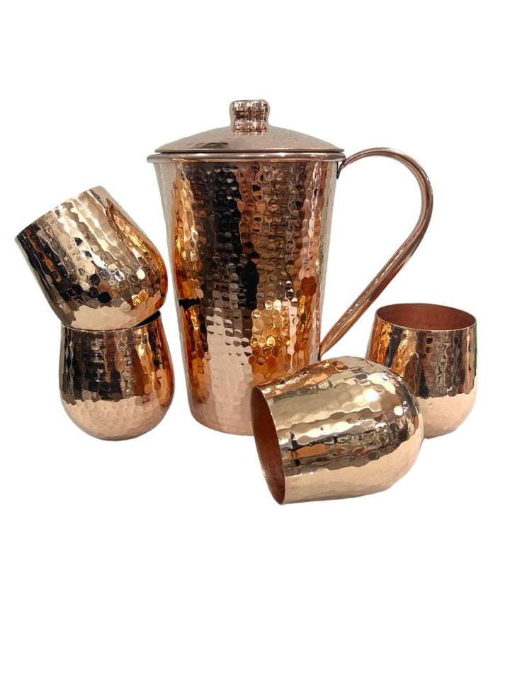 Hammered copper pitcher with lid and four tumblers set, featuring a shiny finish.