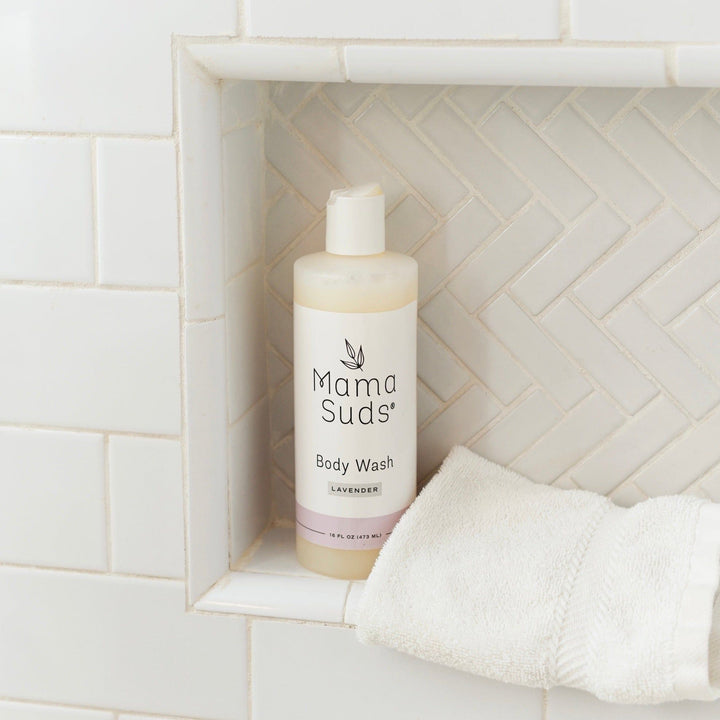 Plant-based lavender body wash bottle on bathroom shelf with white towel
