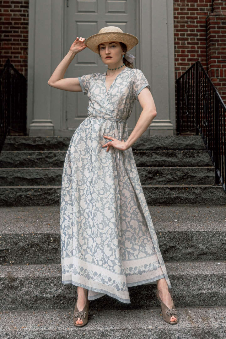 Woman wearing a blue floral maxi wrap dress poses on steps, showcasing elegant and breathable Bemberg crepe fabric for style and comfort.