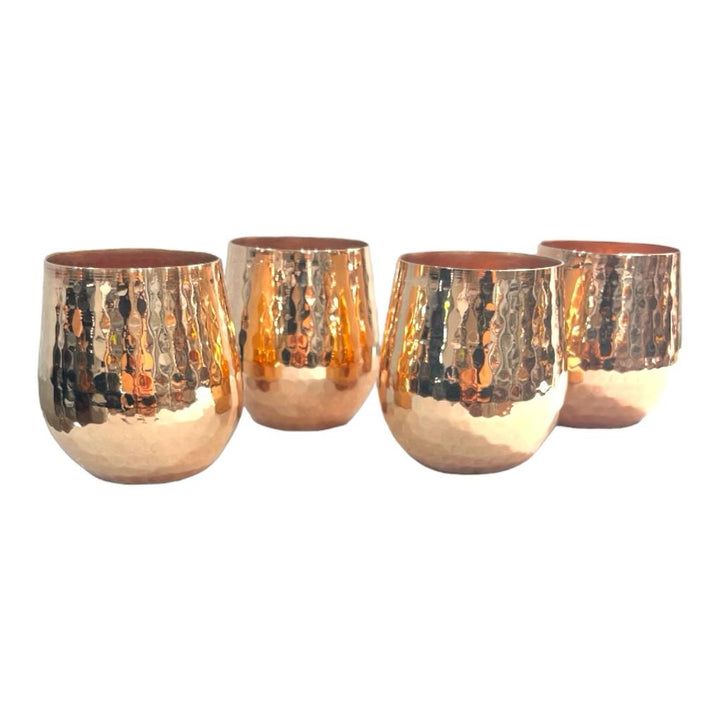 Set of four shiny hammered copper tumblers with textured finish, perfect for serving beverages, enhancing kitchen decor.