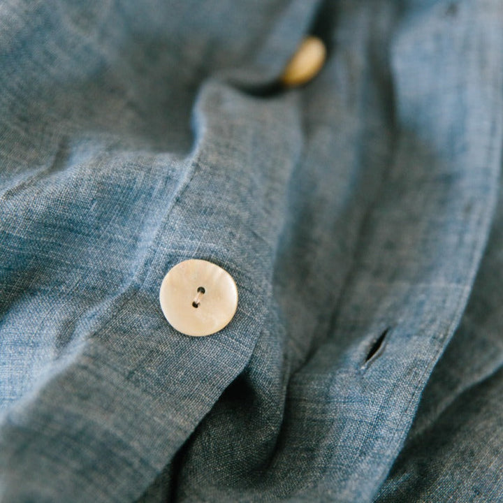 Close-up of a denim blue linen duvet cover from a set, showcasing natural buttons and high-quality Belgian flax fabric.