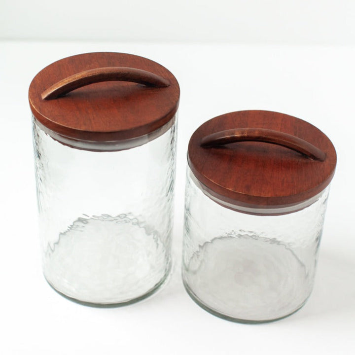 Large clear glass canisters with hand-carved wooden lids, perfect for kitchen storage or apothecary jars, made from recycled glass.