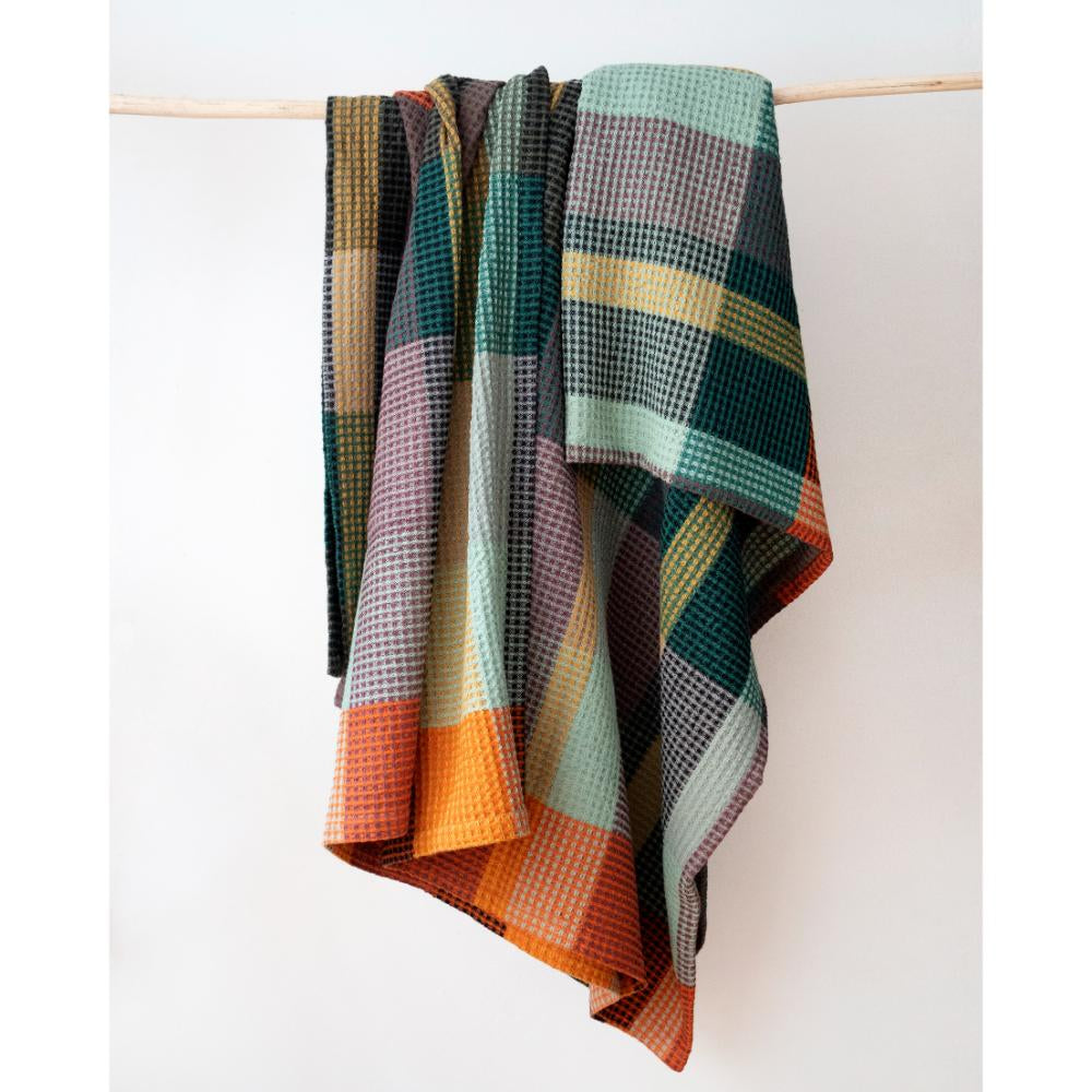 Vrou Vrou Textured Blanket - Cypress, woven in bold patterns with vibrant colors, hanging against a light background.