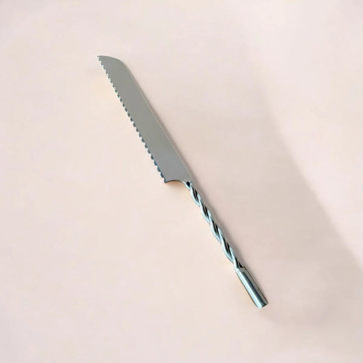 Handcrafted stainless steel serrated bread knife with silver finish on wooden cutting board with artisan loaf