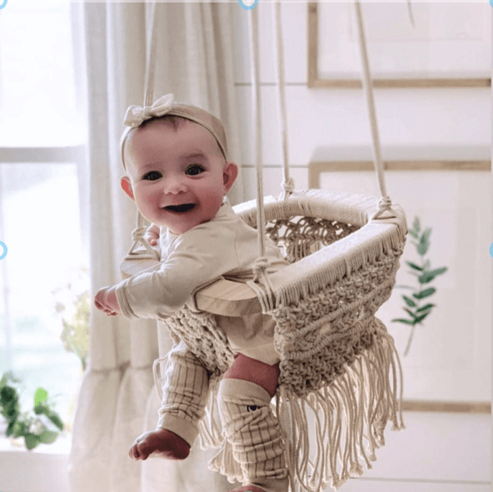 Handwoven organic cotton macrame baby swing with wooden bar and fringe details hanging from ceiling
