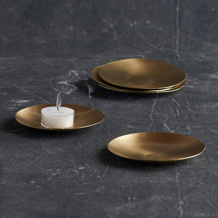 Set of six small handcrafted brass plates with golden finish arranged on neutral surface