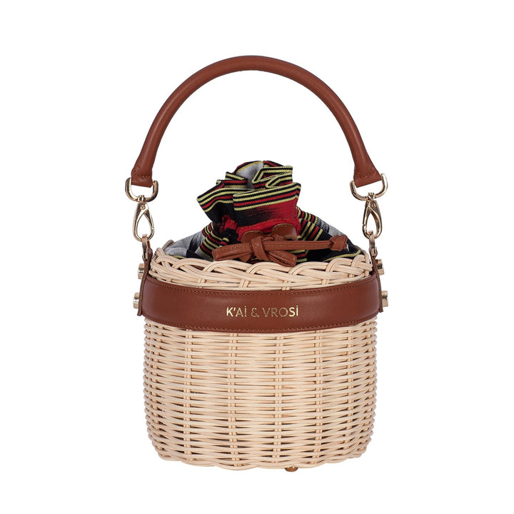 Brown leather and natural straw bucket bag with drawstring closure and striped fabric lining on white background