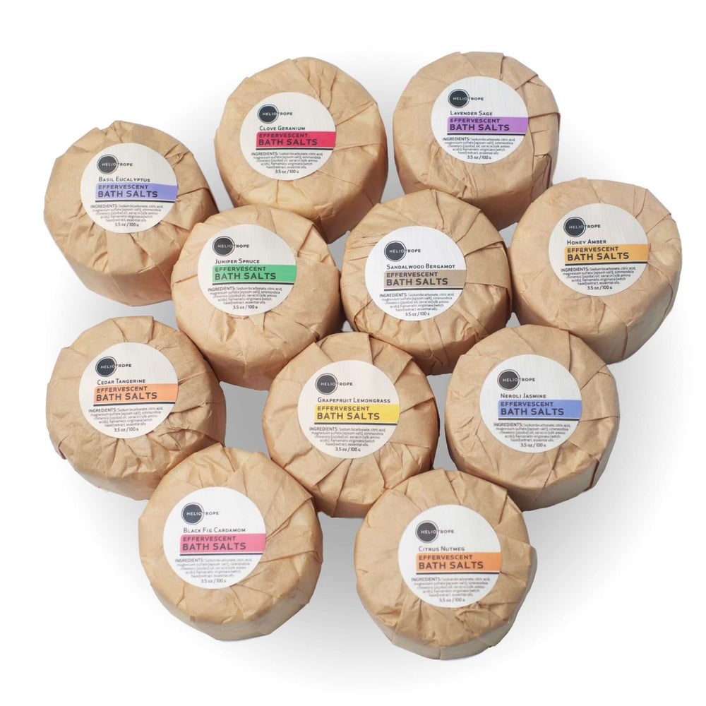 Assorted effervescent bath fizzies wrapped in biodegradable wax paper, enriched with jojoba oil and silk proteins, zero-waste self-care.