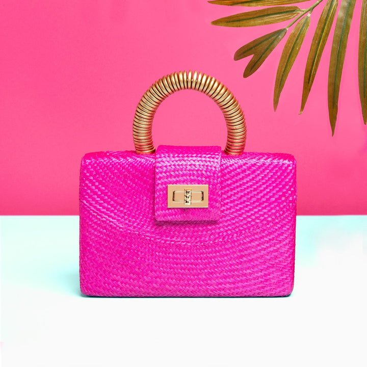 Pink woven buntal straw clutch bag with gold wooden handle and crossbody strap on white background