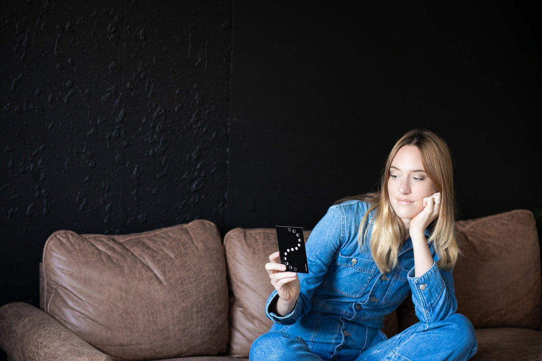Woman on a couch holding Lunar Reflections Mindfulness Card from Moon Phase Deck, enhancing mindfulness and self-awareness.