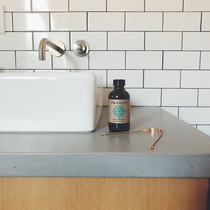 Ayurvedic oral care set with oil pulling bottle and tongue cleaner on a bathroom counter.