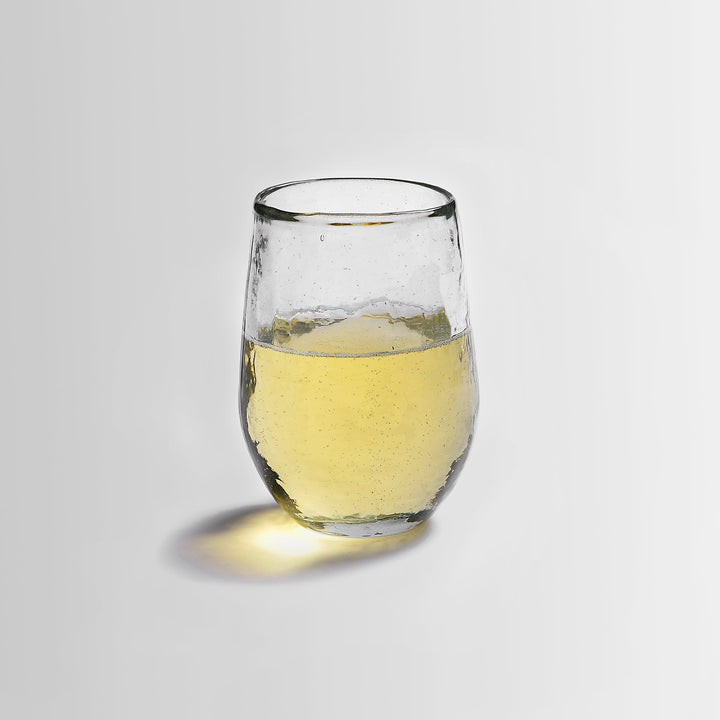 Set of four clear glass tumblers with hammered pebbled texture sitting on wooden surface