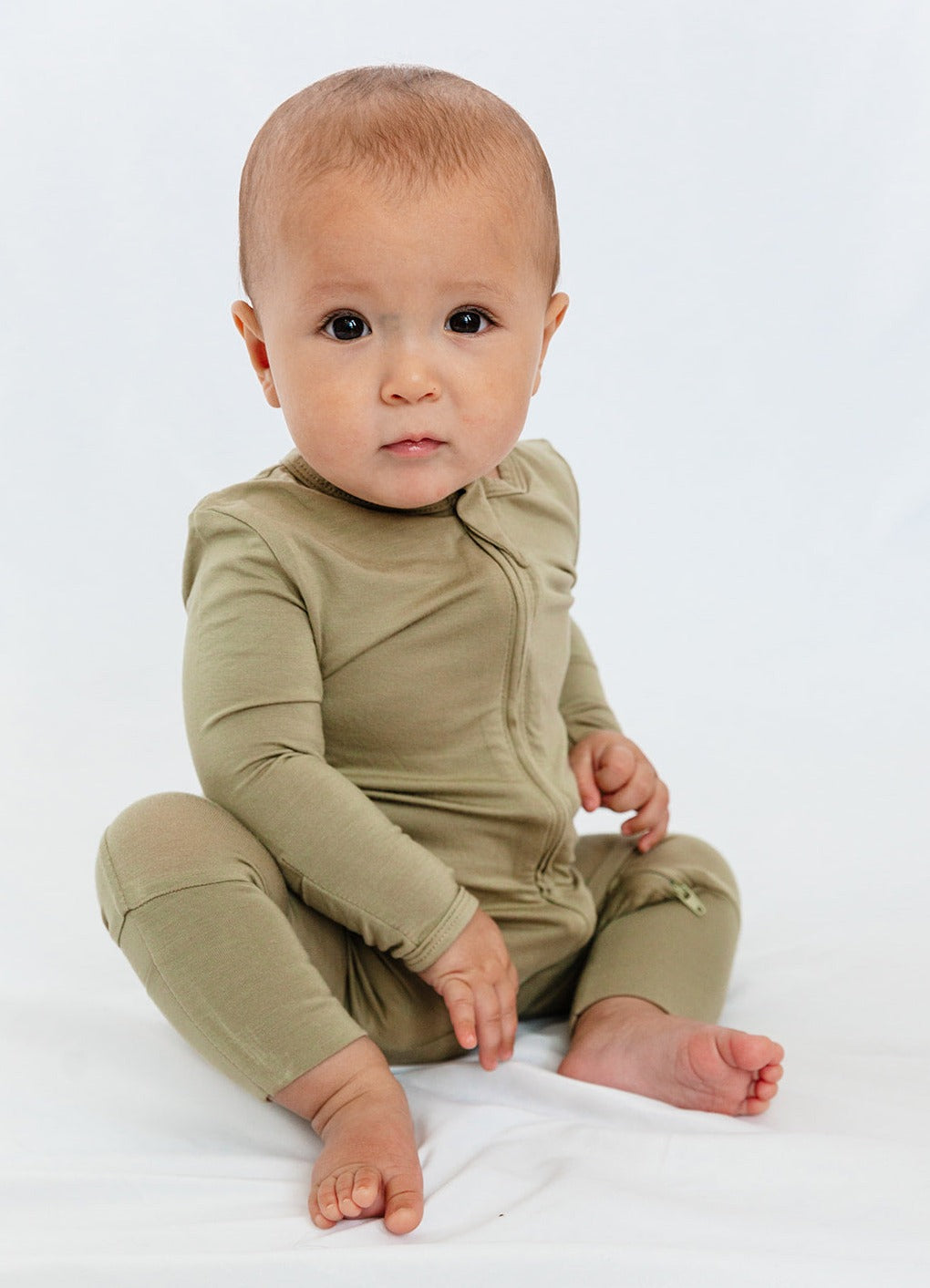 Baby wearing Luxe Bamboo Baby Pajamas in Moss Green, showcasing soft, smooth, antimicrobial fabric with fold-over mittens and two-way zipper.