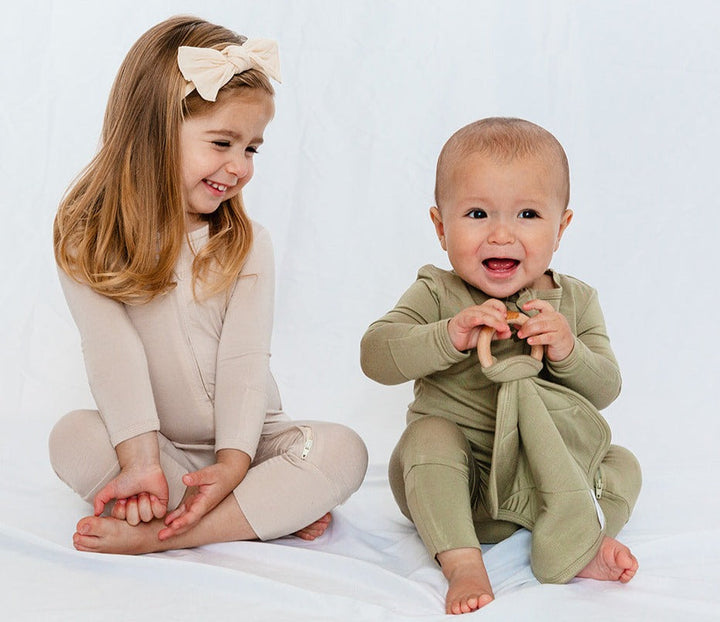 Two smiling children wearing LUXE Bamboo Footless Rompers, showcasing soft and breathable fabric with zippered design for easy diaper changes.