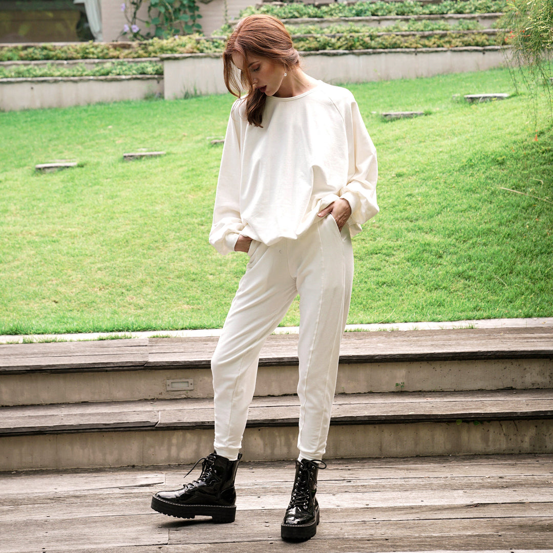 Woman wearing Cameron Bamboo Joggers in off-white fleece, standing on steps with greenery background, showcasing comfort and style.