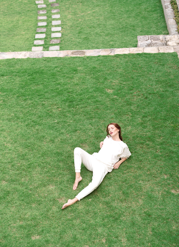 Woman relaxing on grass wearing off-white Cameron Bamboo Joggers, showcasing comfort and style.