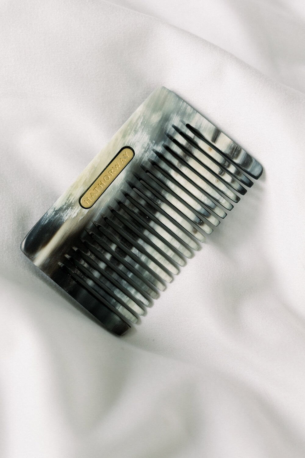 Pocket-sized Chai Buffalo Horn Comb on white fabric, ideal for hair and beard grooming, made from ethically-sourced materials.