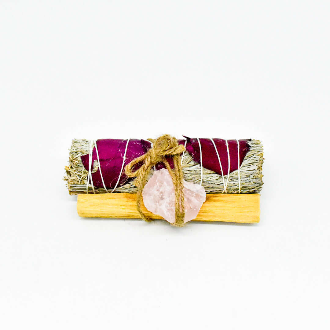 White sage smudge stick bundle with red rose petals, palo santo, and rose quartz for love and friendship rituals.