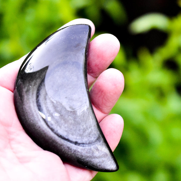 Polished silver sheen obsidian crescent moon stone with natural shimmer against white background
